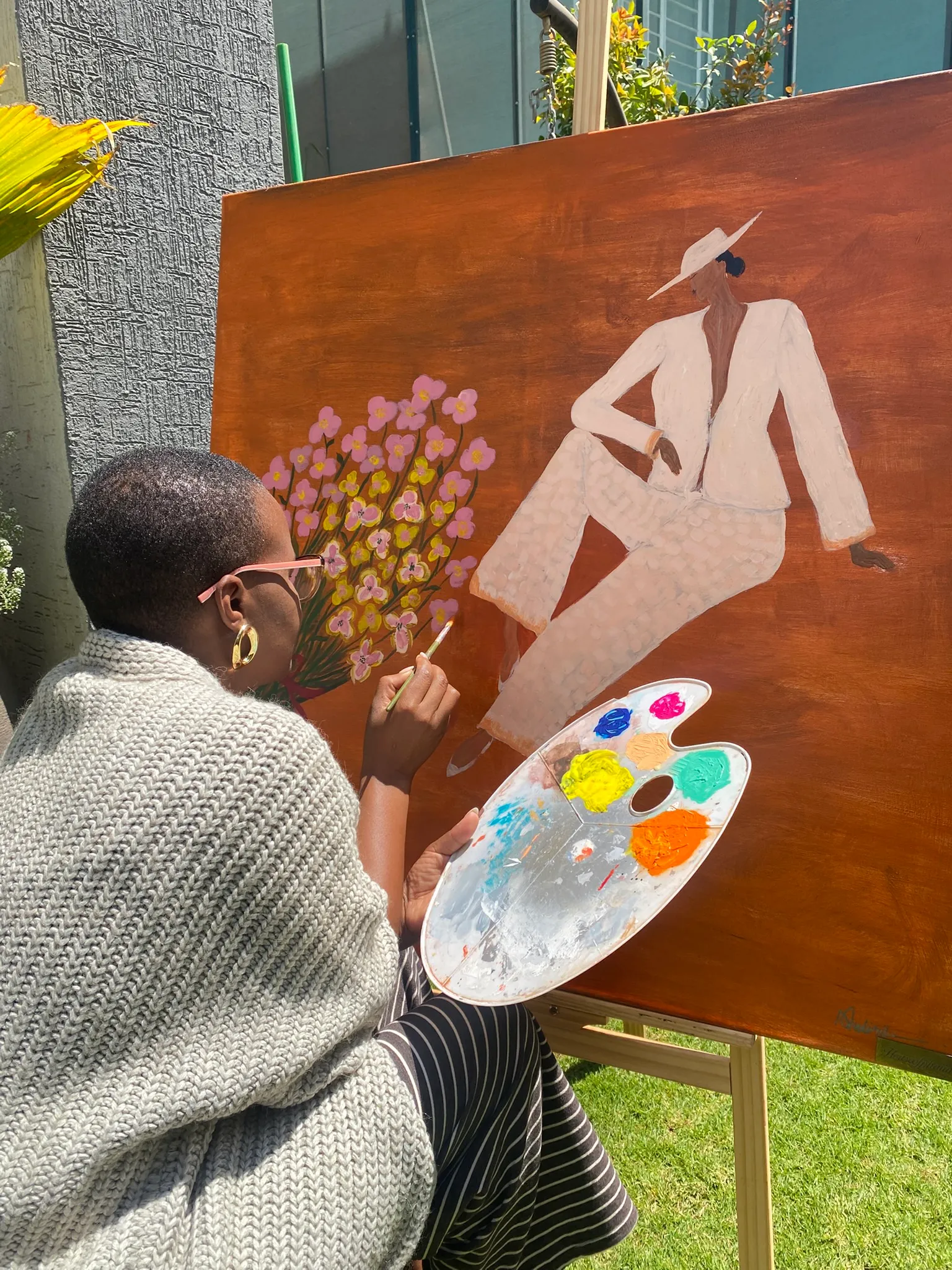 Nelly at her easel, holding a palette while working on a painting in the studio
